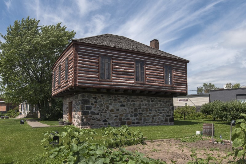 Ermatinger Clergue National Historic Site blockhouse; a stately rough wood building with tall windows sitting on a stone and mortar foundation.