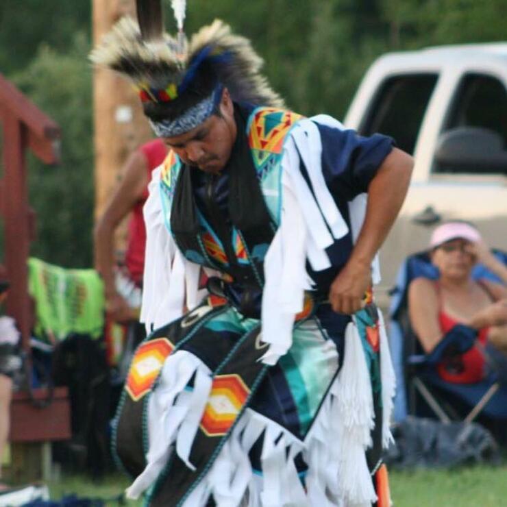 a focused man in beautiful regalia dances in front of spectators at a pow wow.