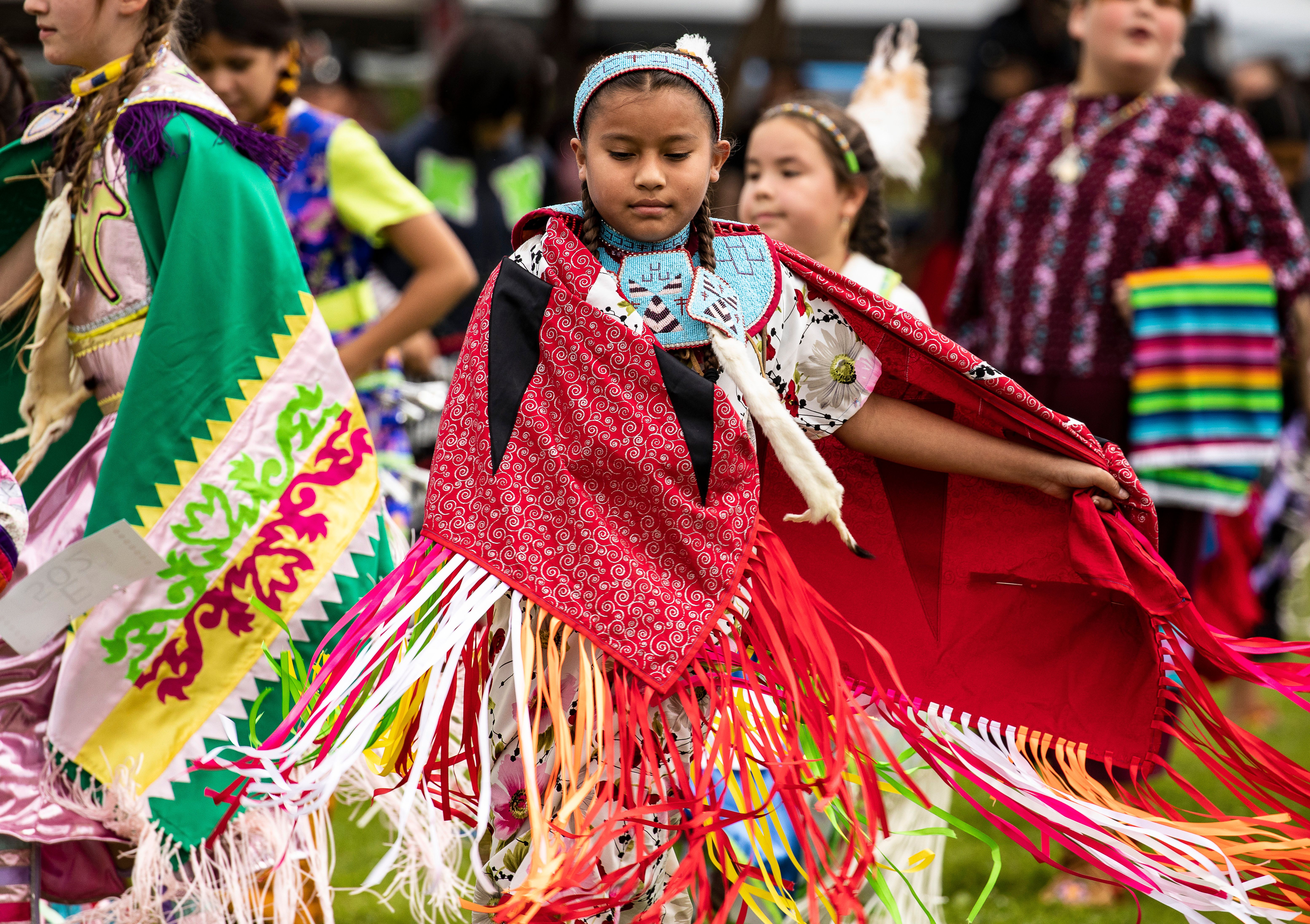 two girls with fancy shawls dance at a pow wow.