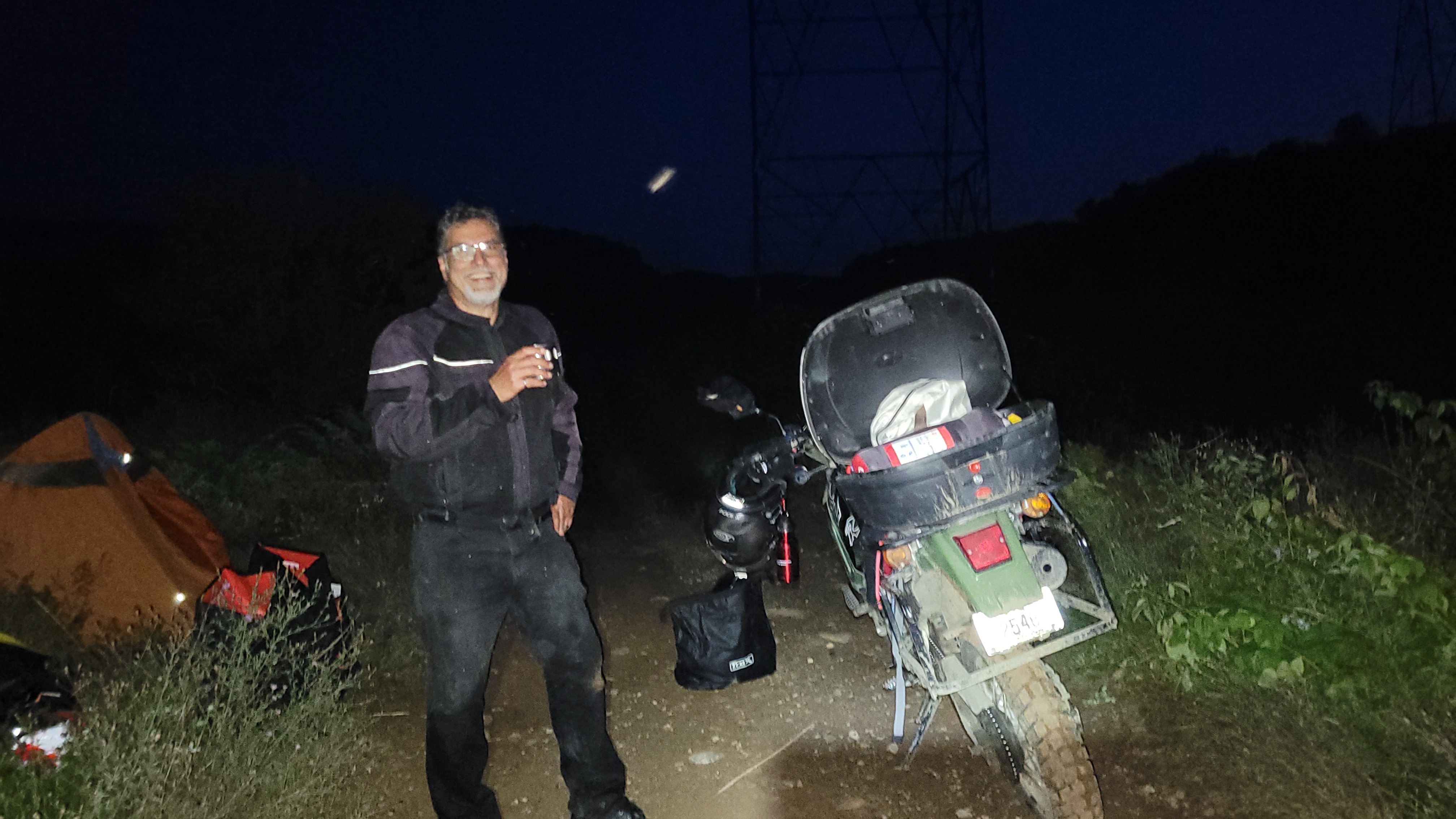 A man in motorcycle gear next to a bike at night.