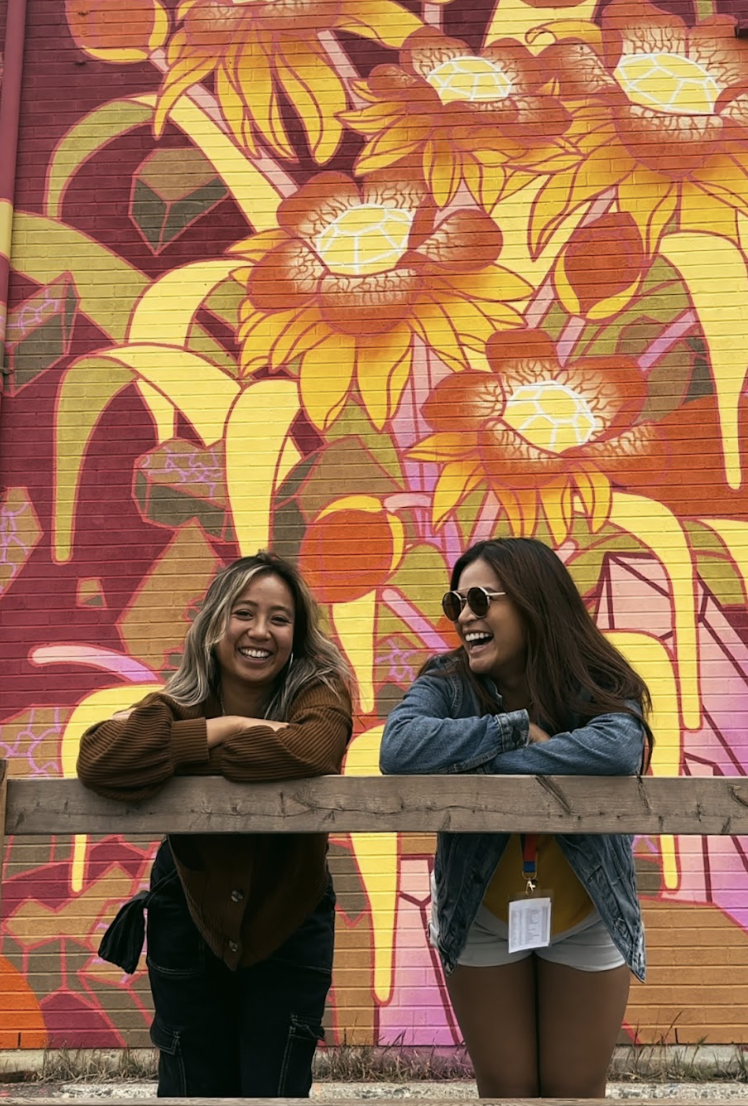 Two women laugh in front of a mural during Up Here Fest in Sudbury