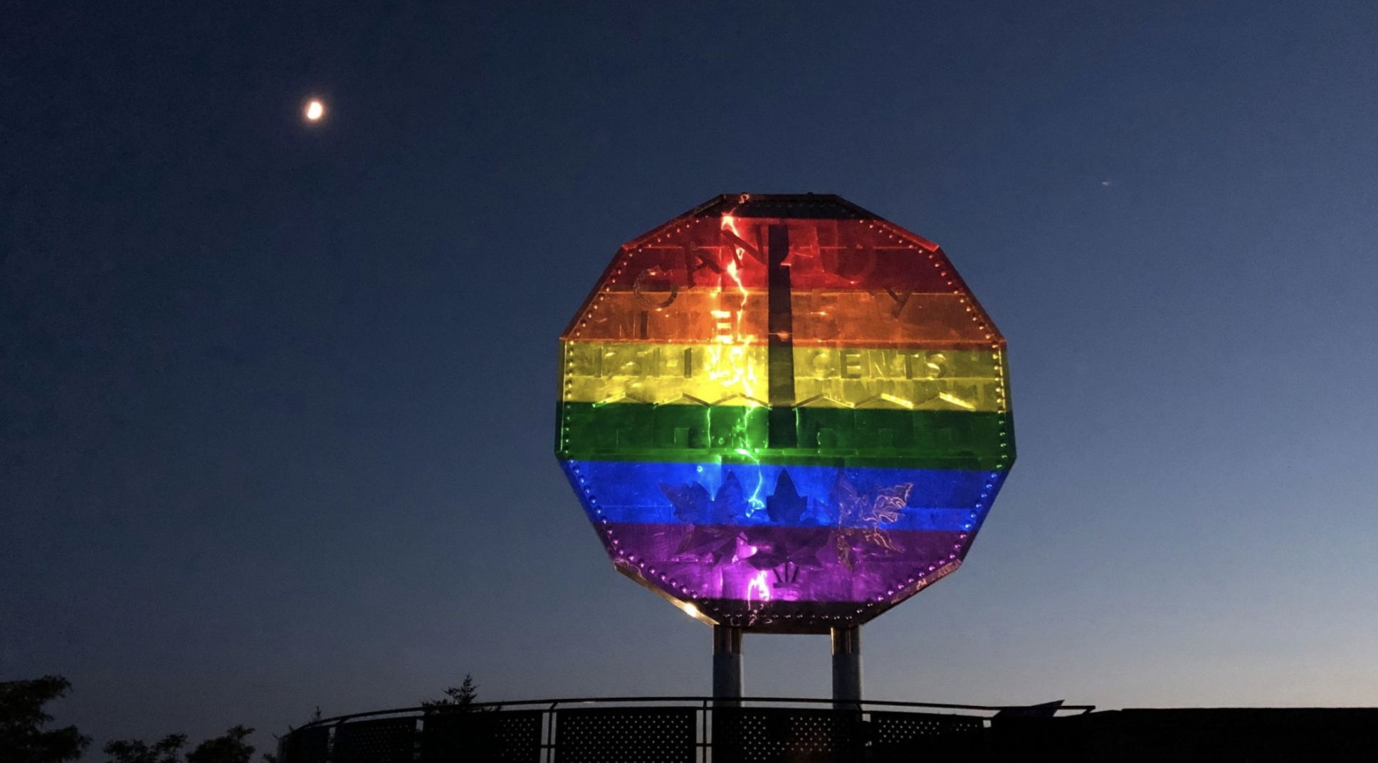 Sudbury's Big Nickel lit up in a rainbow of colours at night