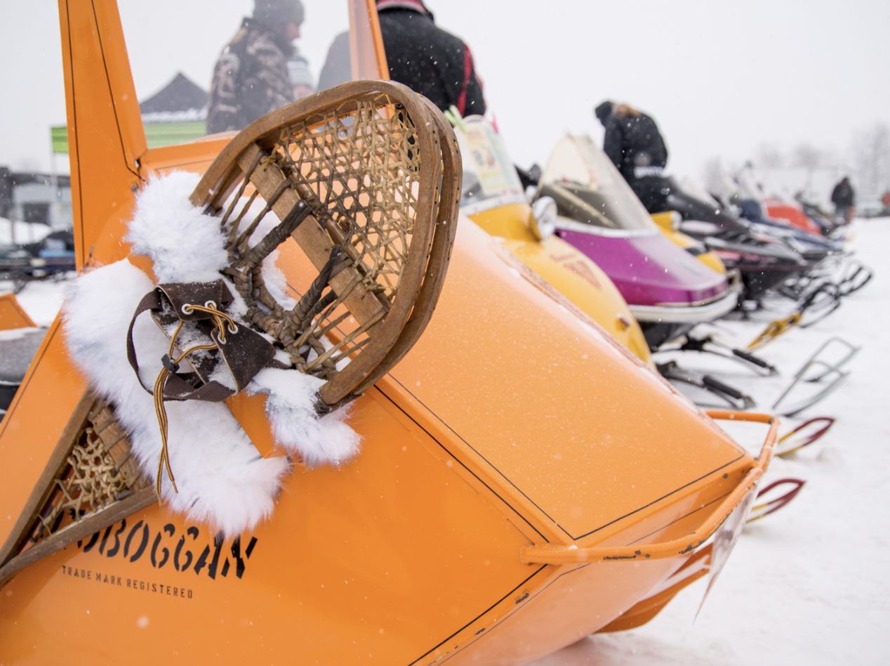 A line up of vintage snowmobiles against a snowy field