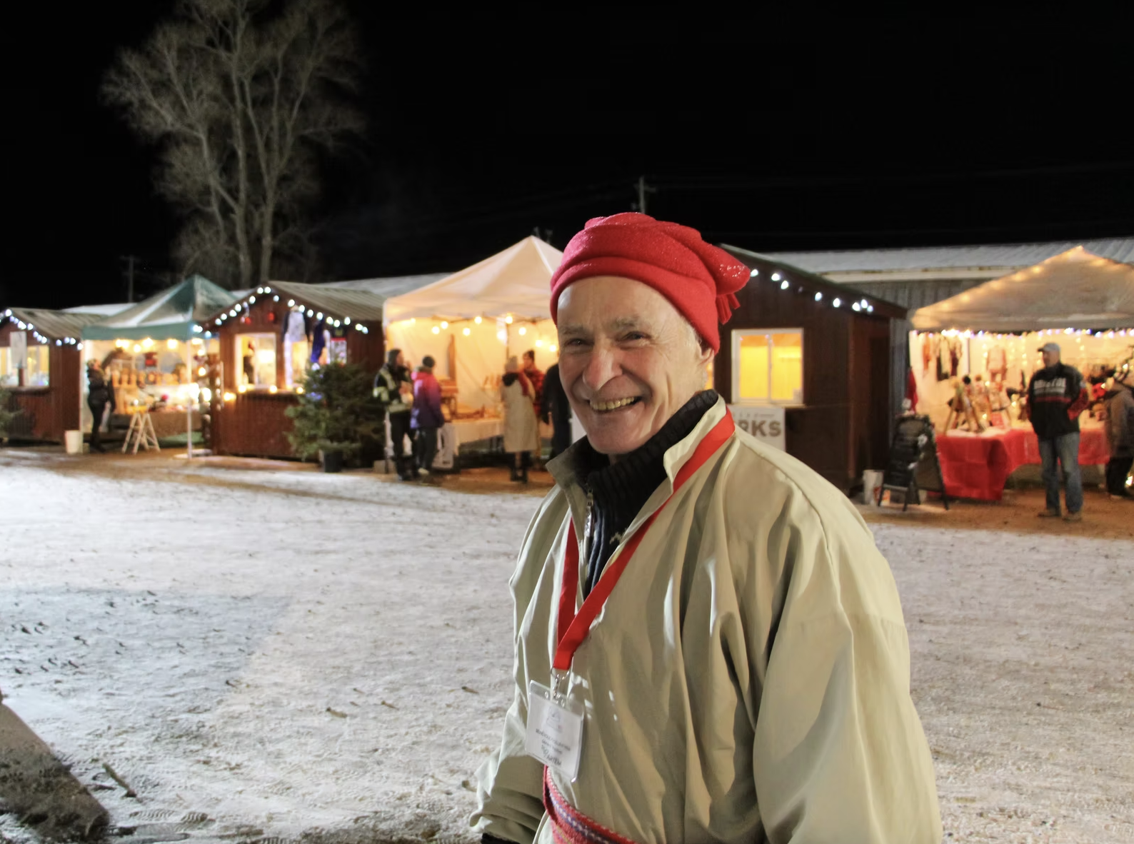 An older white man dressed in 17th century clothing smiles in front of the holiday market stalls