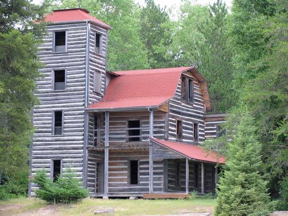 The White Otter Castle; a multi-level log mansion with covered porch, arched roof and a tall tower on on corner. It sits in the middle of a lush forest.