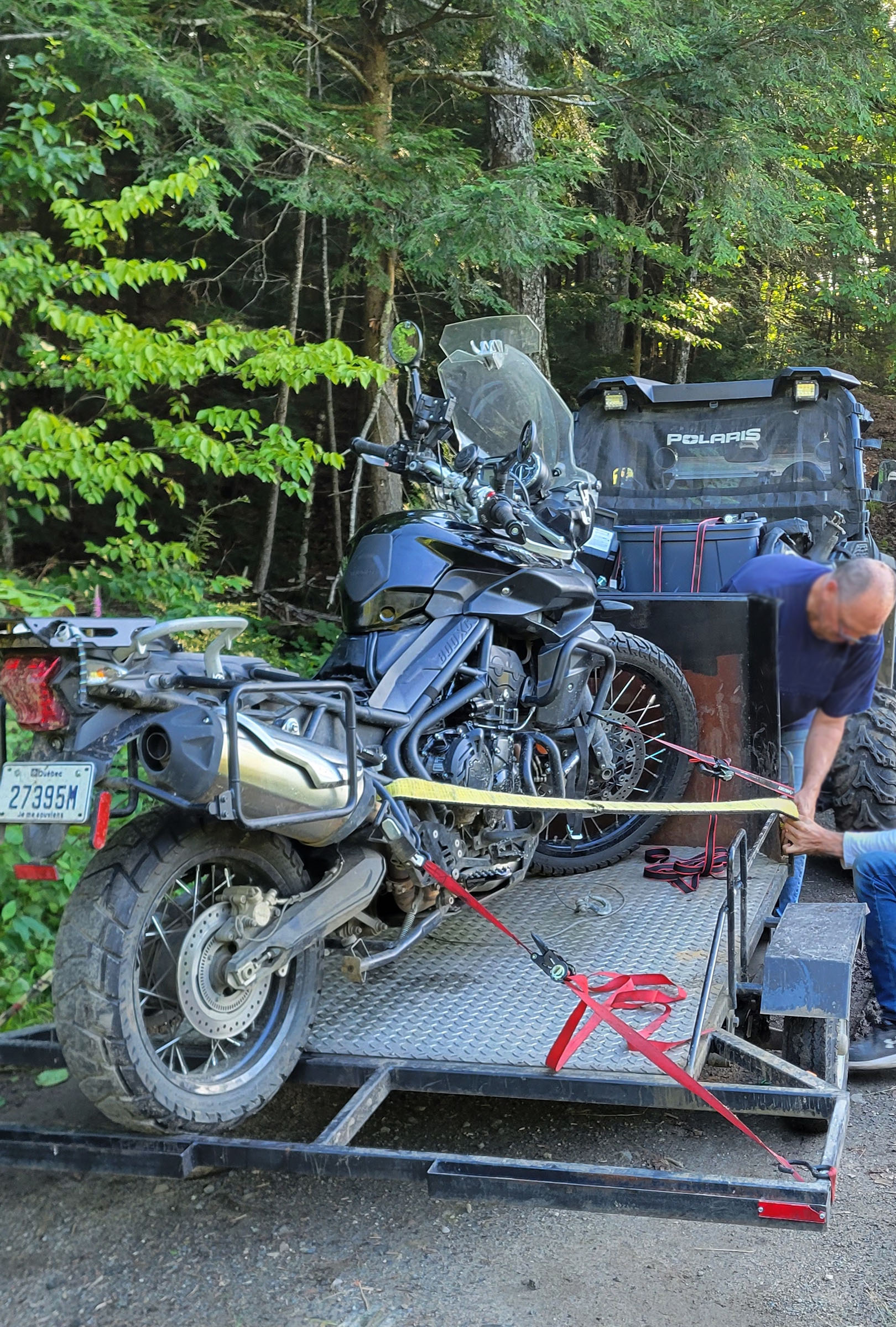 A motorcycle being hoisted onto a trailer in the bush.