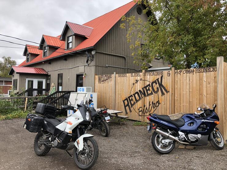 motorcycles parked outside a large, tidy building with a red roof and a wooden fence that says "Redneck Bistro" on it.
