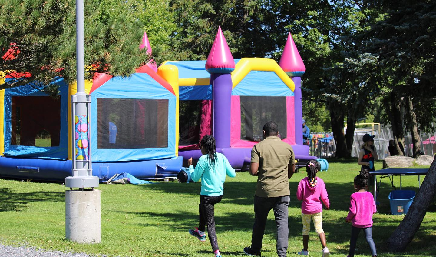a family walks up to a row of inflatable bouncy castles in an outdoor park in Sudbury.