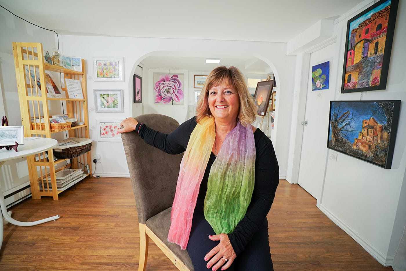a smiling Carmen Martortella sits in a tidy gallery surrounded by watercolour paintings.
