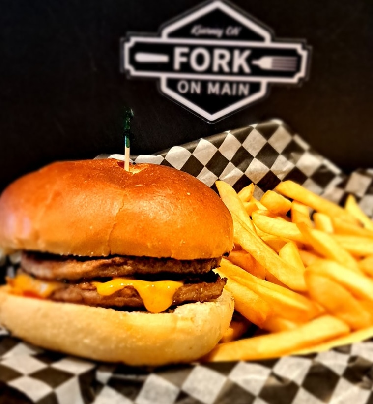 A hamburger and fries in a basket with a sign above that says "Fork On Main".