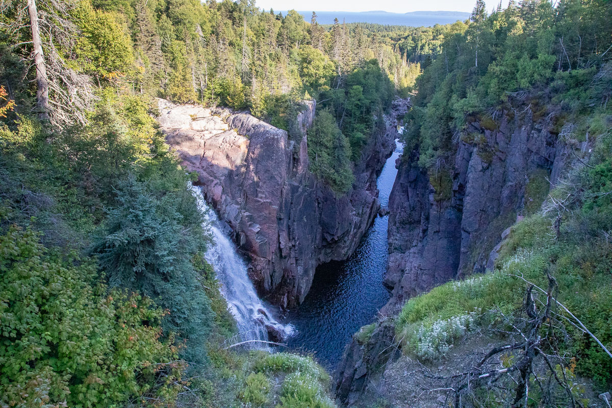 Aguasabon Falls; a tall waterfall plunging sharply into a steep rock gorge surrounded by green boreal forest.