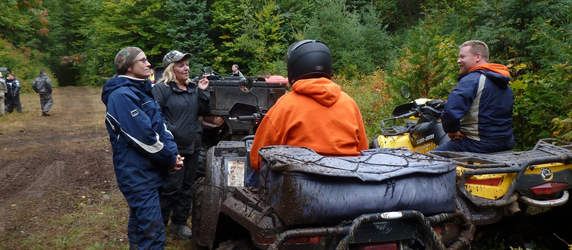 a group of riders stand around an ATV, talking and laughing.