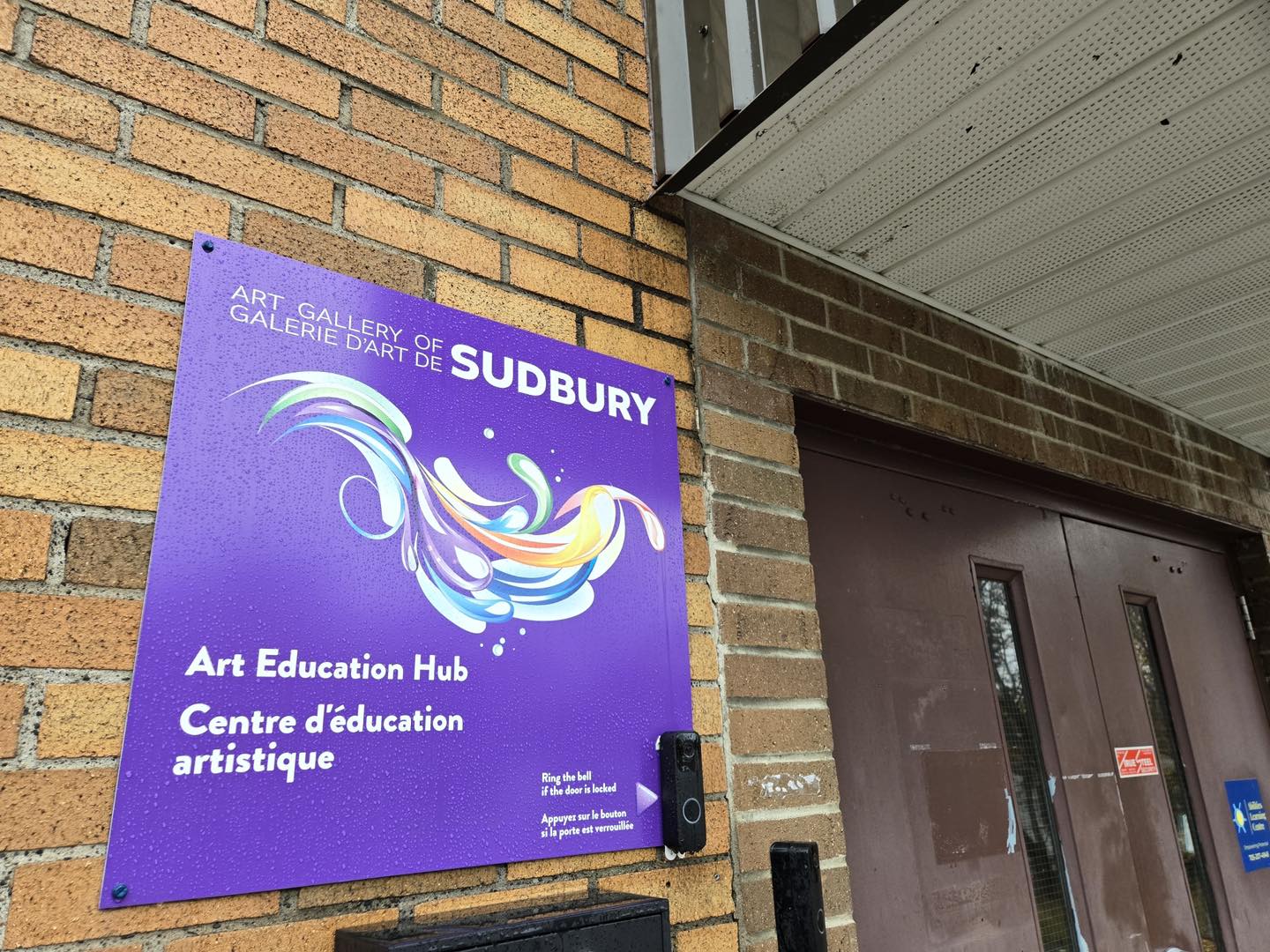 a purple and rainbow sign on the side of a building that reads "Art Gallery of Sudbury Art Education Hub".