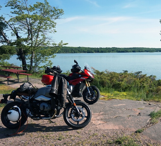 motorcycles parked next to a forest lake in Algoma Country on summer day.