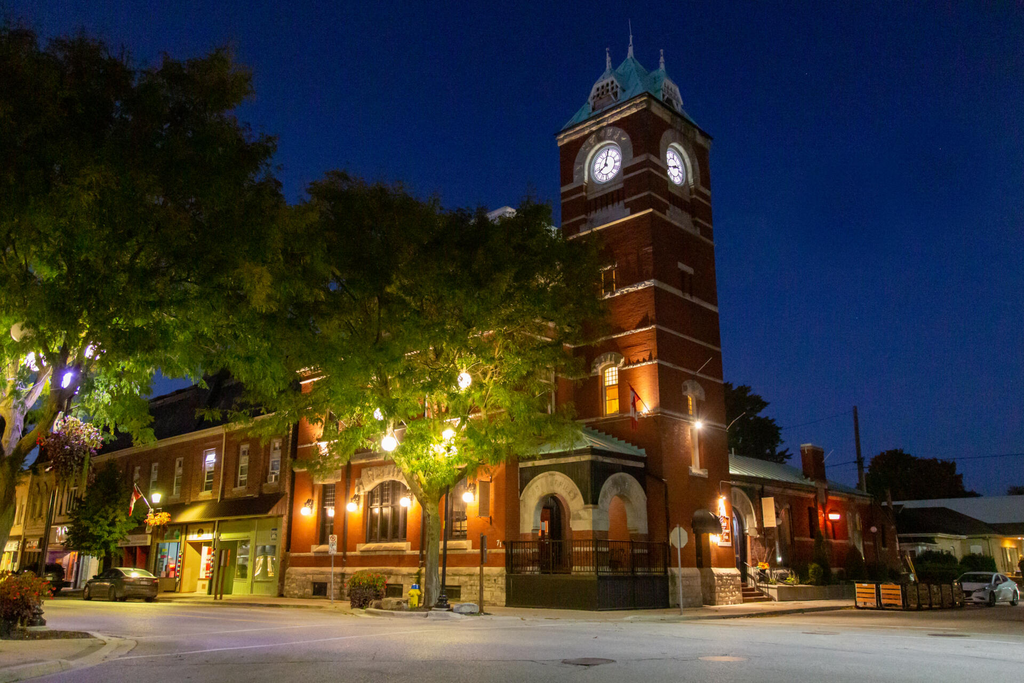 The Clocktower Inn; a beautiful historic brick clock tower turned Inn, surrounded by lush green trees and lit up on a summer night.