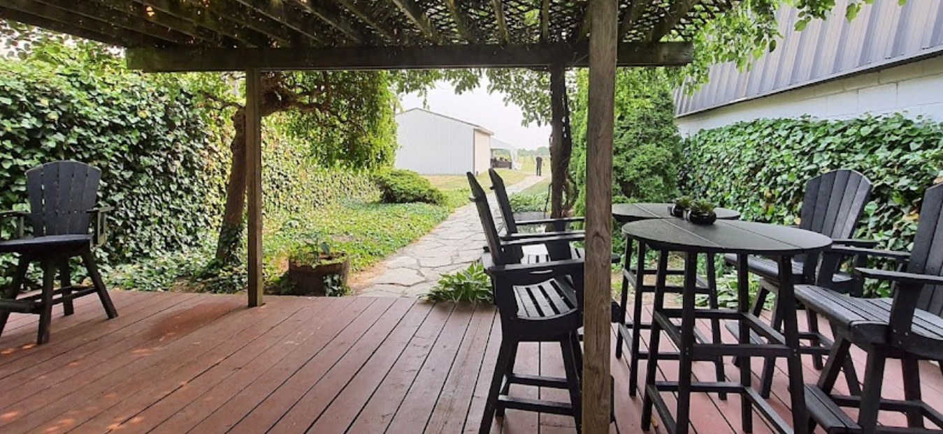 a covered wooden patio with tables and chair surrounded in greenery and vines