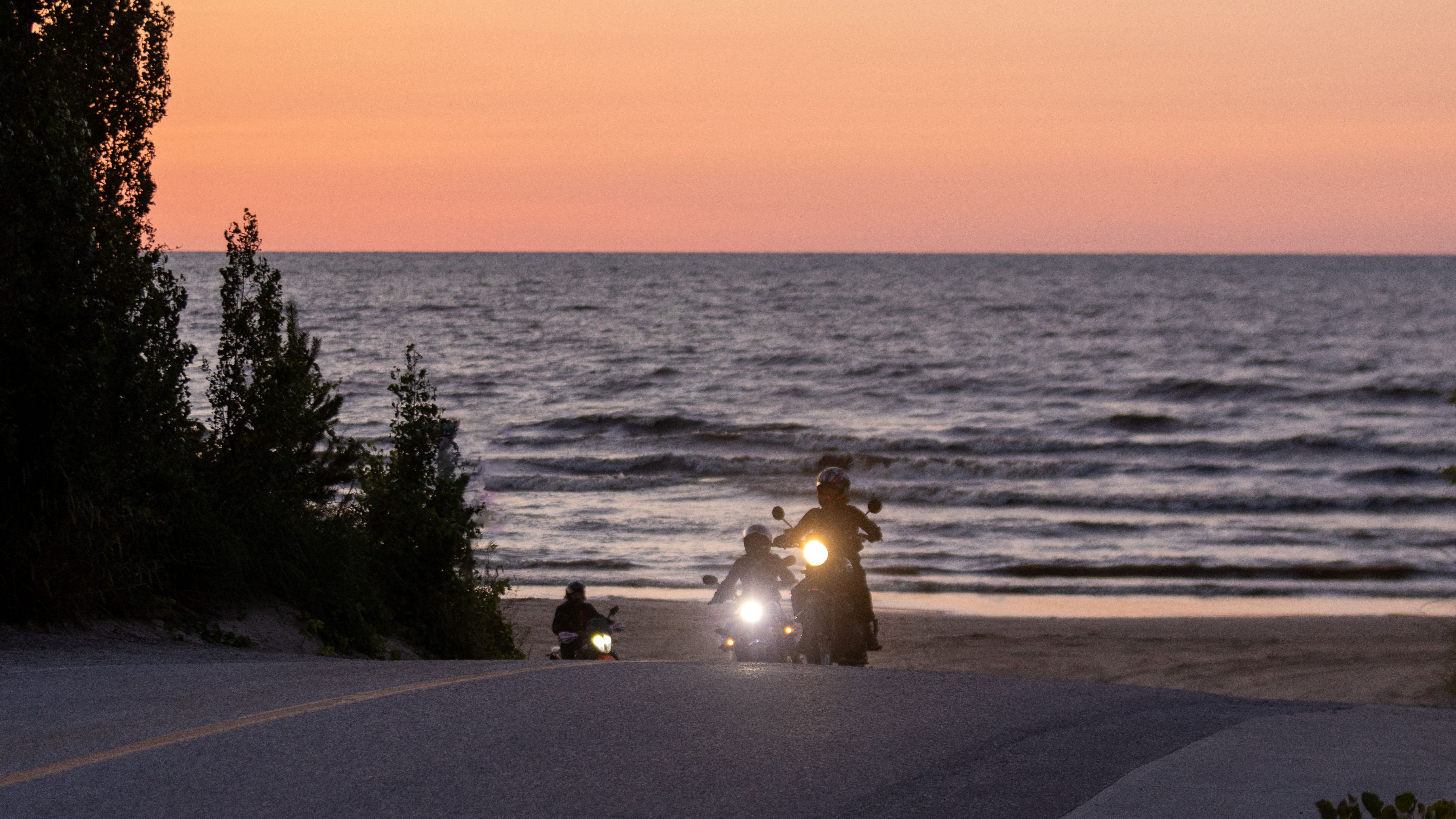 motorcyclists ride along a smooth beachfront highway at sunset by Lake Huron.