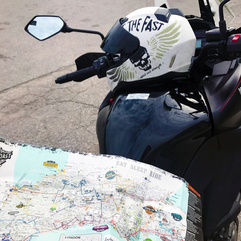 a motorcyclist holds a map of the Cruise the Coast route while parked at the side of a road.