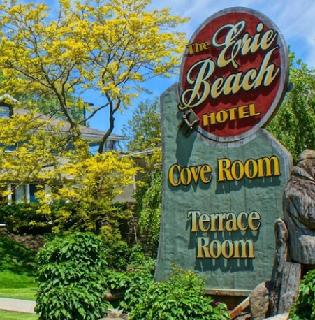 The Erie Beach Motel and sign surrounded by lush greenery under a blue sky.
