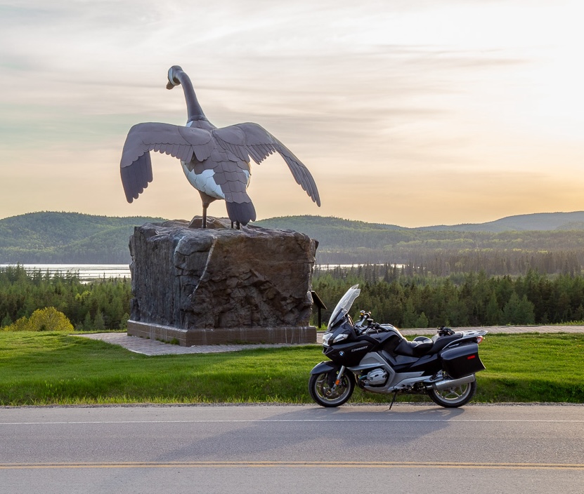 a motorcycle parked next to the Wawa Goose statue at sunset on a summer day.