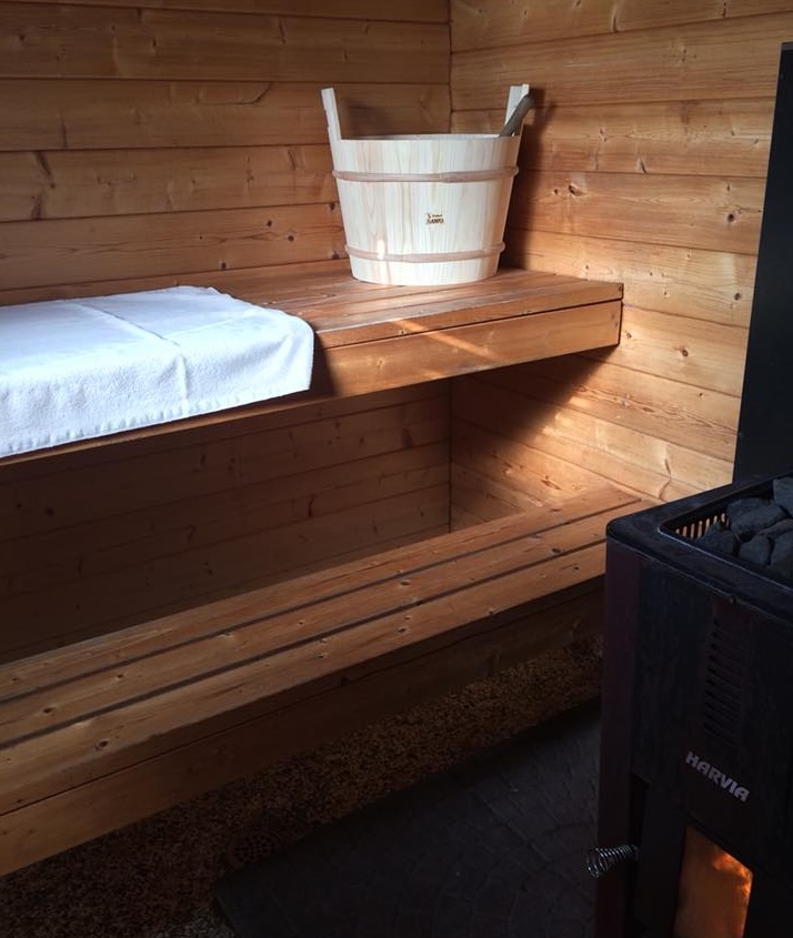 a wooden sauna with glowing iron stove, white towels and a wooden water bucket inside.