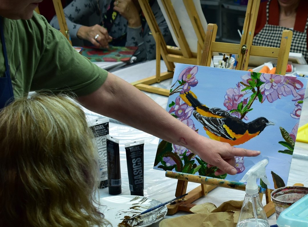 an instructor points and talks about student's painting at a group painting session.