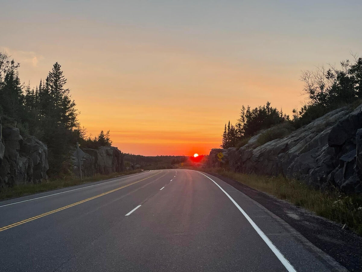 an orange sunset over an open paved forest highway near Kenora.
