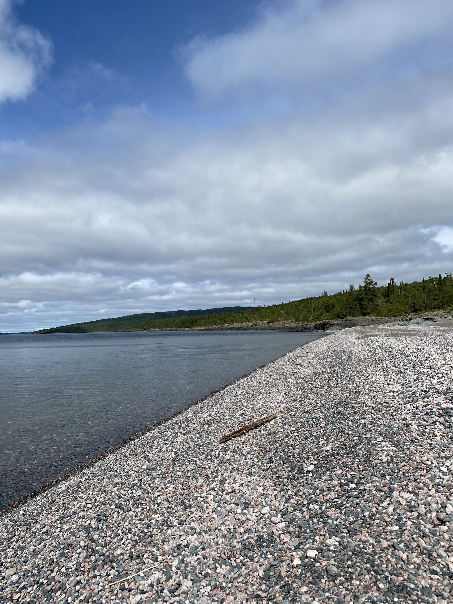 Schreiber Beach; a pebble beach with glassy lake water and boreal forest at the skyline.