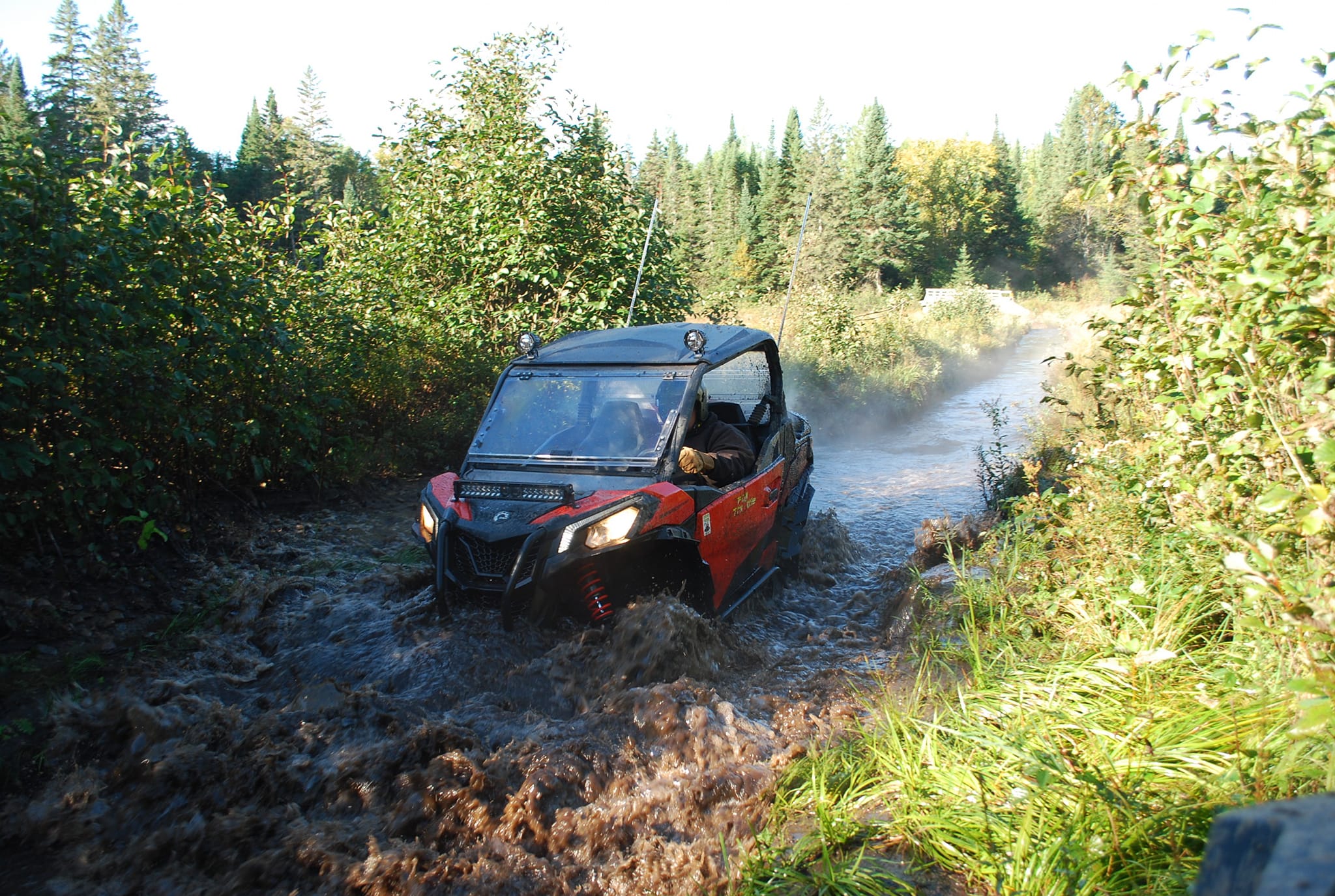 a UTV drives through a deep stream in the middle of a grassy, treed field.