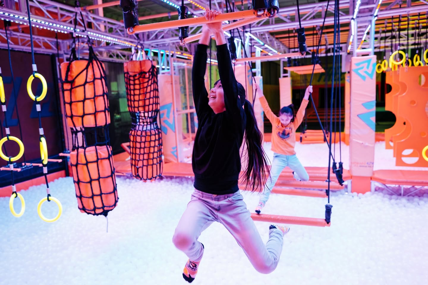 kids swing across a series of rings illuminated by blacklight at the Urban Air Adventure Park.