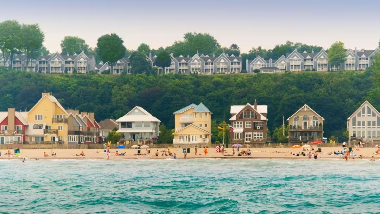 a sandy beach filled with people along turquoise water, backed with green trees and beach houses.