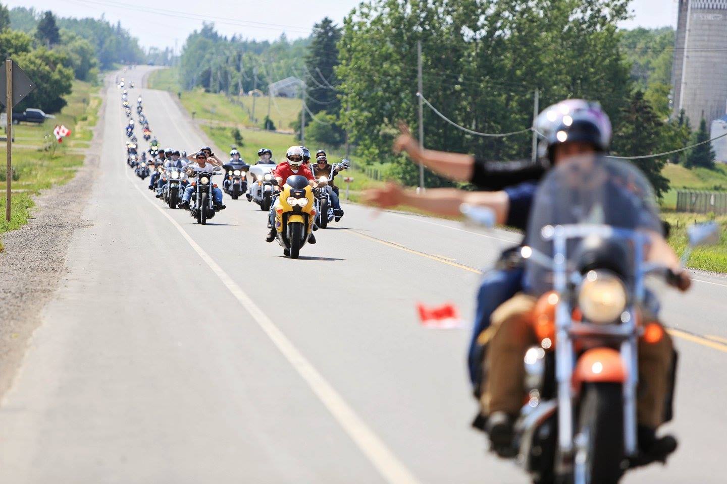 a procession of motorcyclists parading down the highway, extending into the distance, on a summer day.