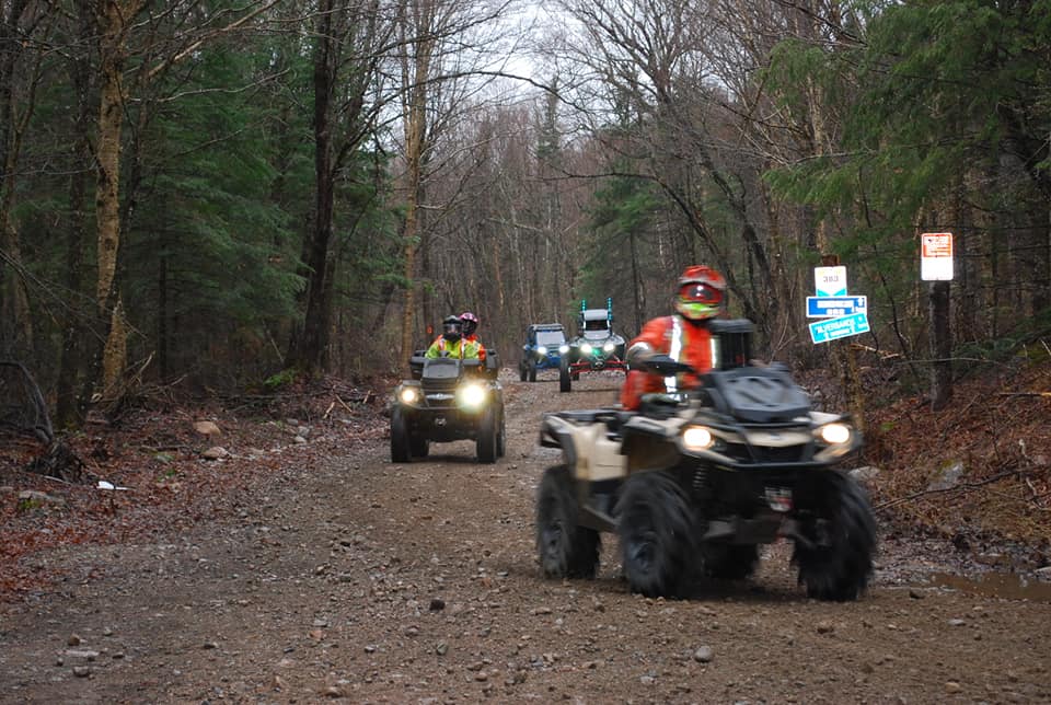 a group of ATVers ride along a muddy forest trail on a rainy spring day.