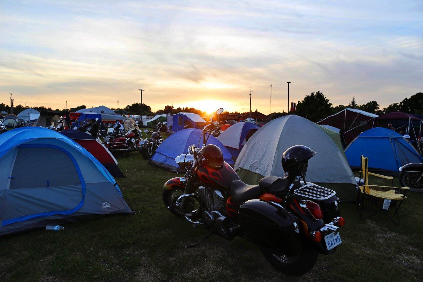 a field of tents and motorcyles at sunset on a summer evening.