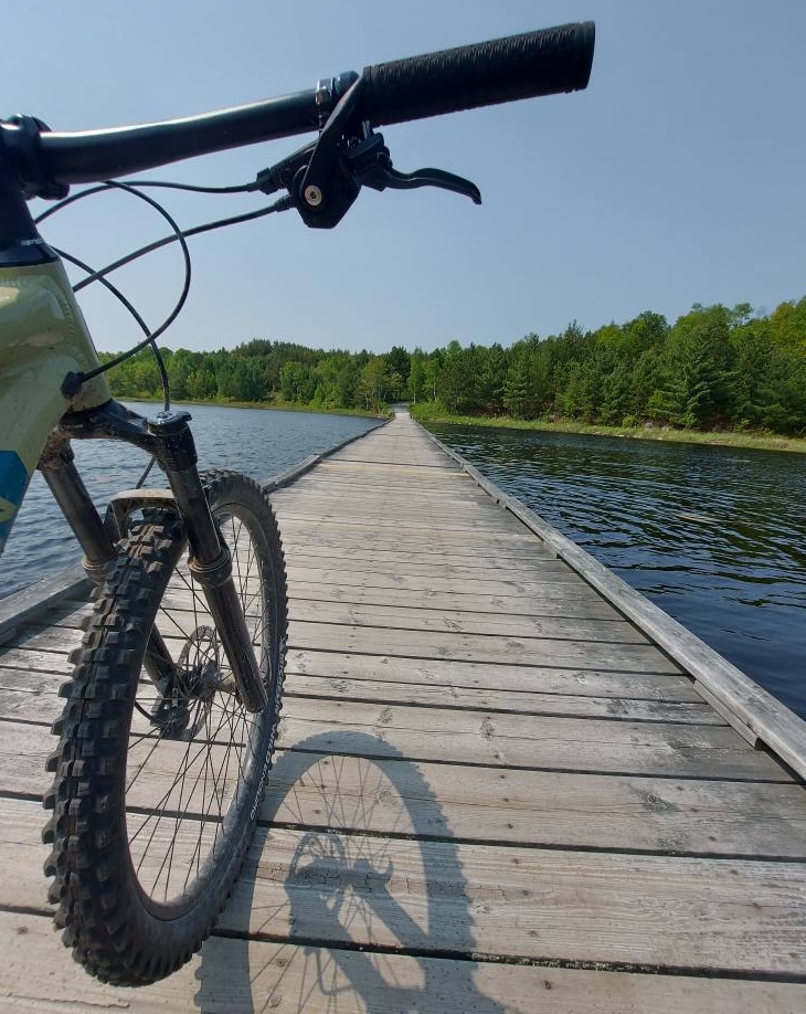 Lake Laurentian Conservation Area; a bike wheeling down a boardwalk across a lake, stretching off toward a forest in the distance.