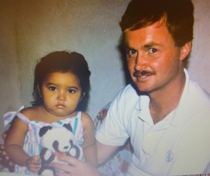 Barry Phippen, smiling proudly next to his newly adopted daughter Justine, a very young, dark-eyed Honduran girl holding a stuffed panda.