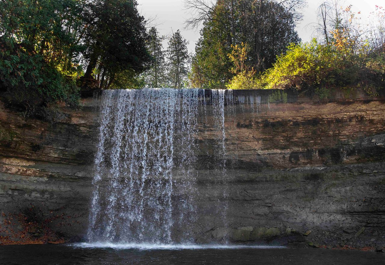 Bridal Veil Falls; a gentle curtain of water that falls over a steep rock cliff into a quiet pool in the forest.