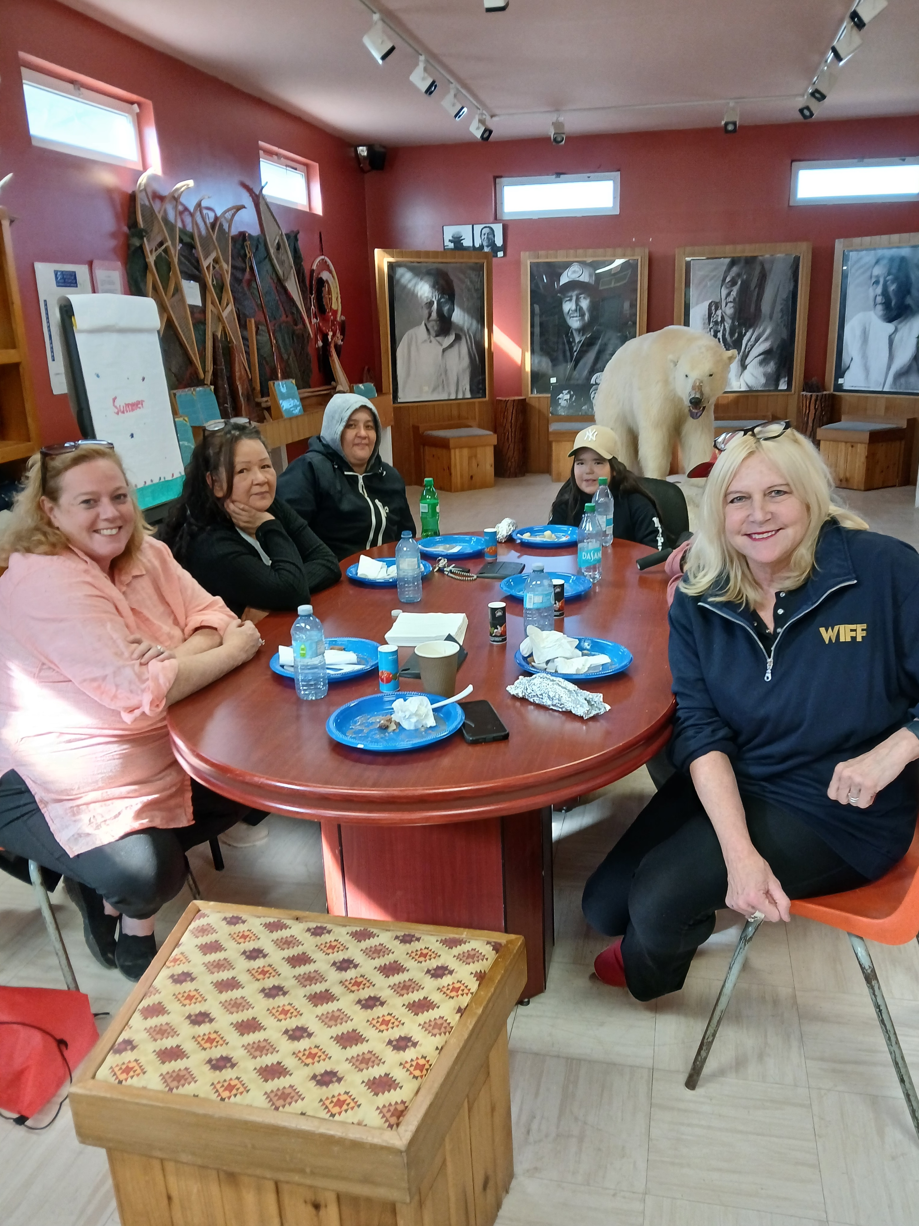 Susan Truppe and Lisa MacLeod sit at a table in with several representatives of the Cree Cultural Interpretive Centre. All are smiling and sitting around a large table in a room filled with large black and white photographs.