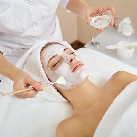 a woman wrapped in white towels gets a facial at a spa.