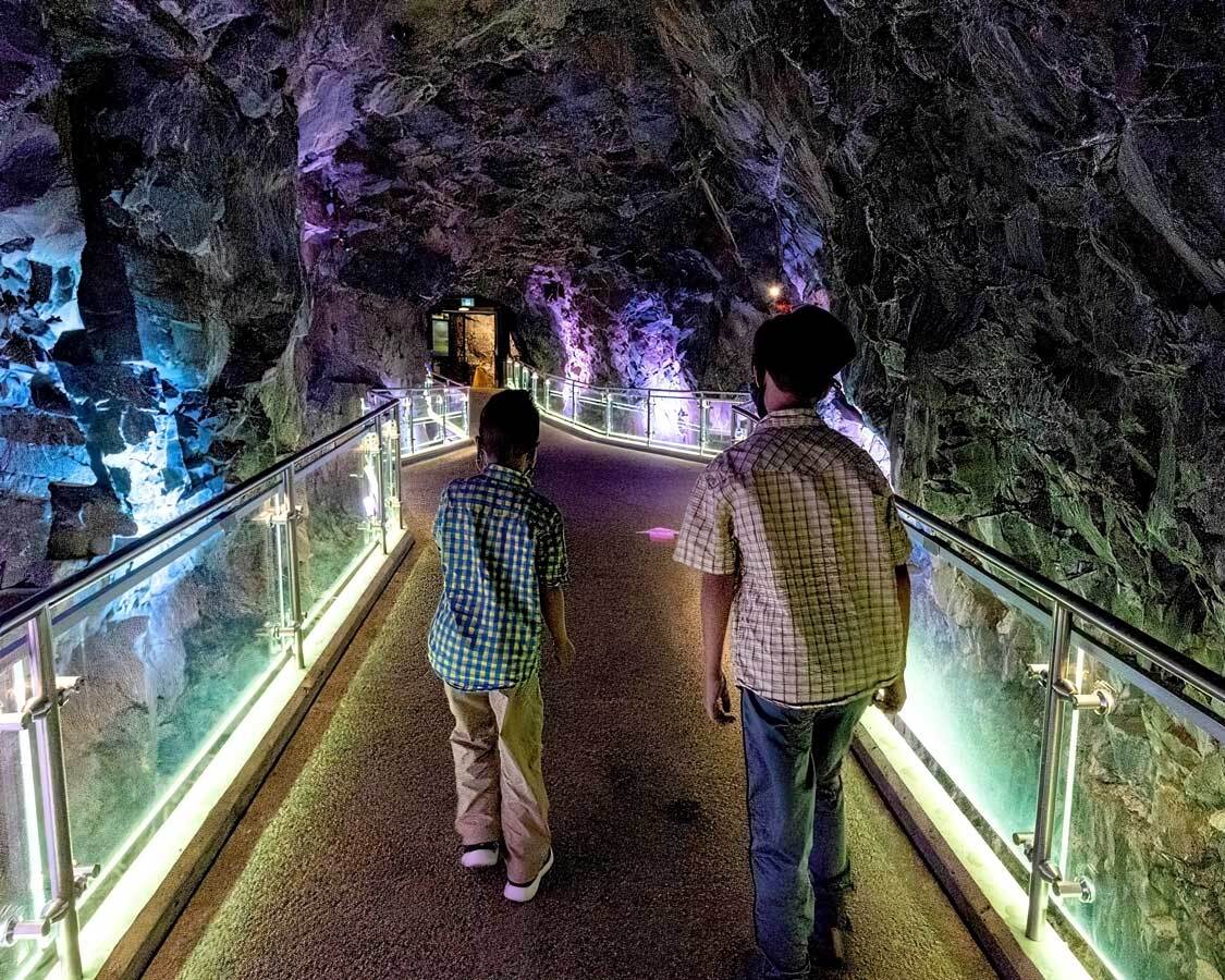 kids walking over an illuminated bridge through a rock tunnel at Science North in Sudbury.