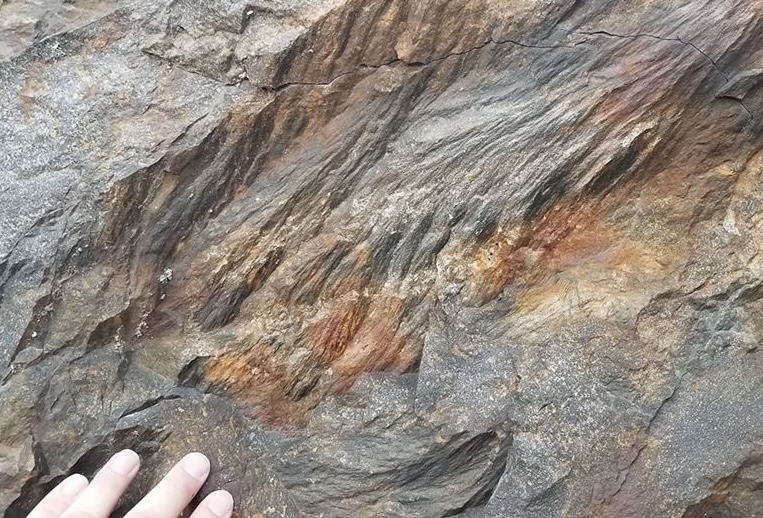 a hand touches a large piece of rock showing the ridged and varigated pattern of a shatter cone.