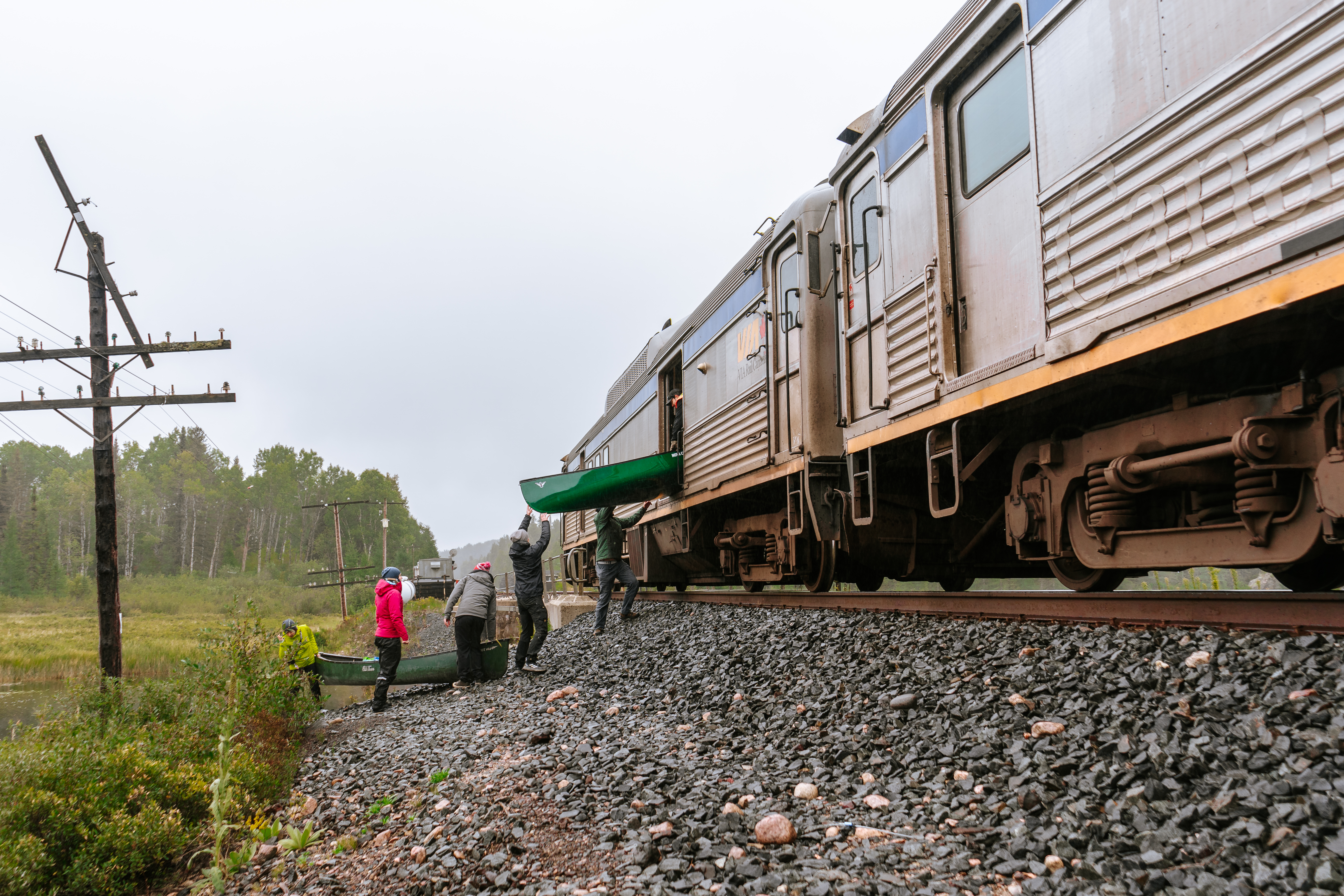 a group of people unloading a canoe from a train car on a track surrounded by green forest. 