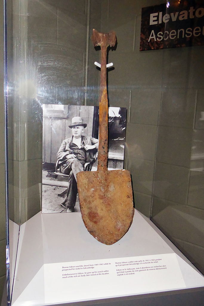 a rusted shovel once owned by Thomas Edison, in a glass display case with a black and white photo of him.