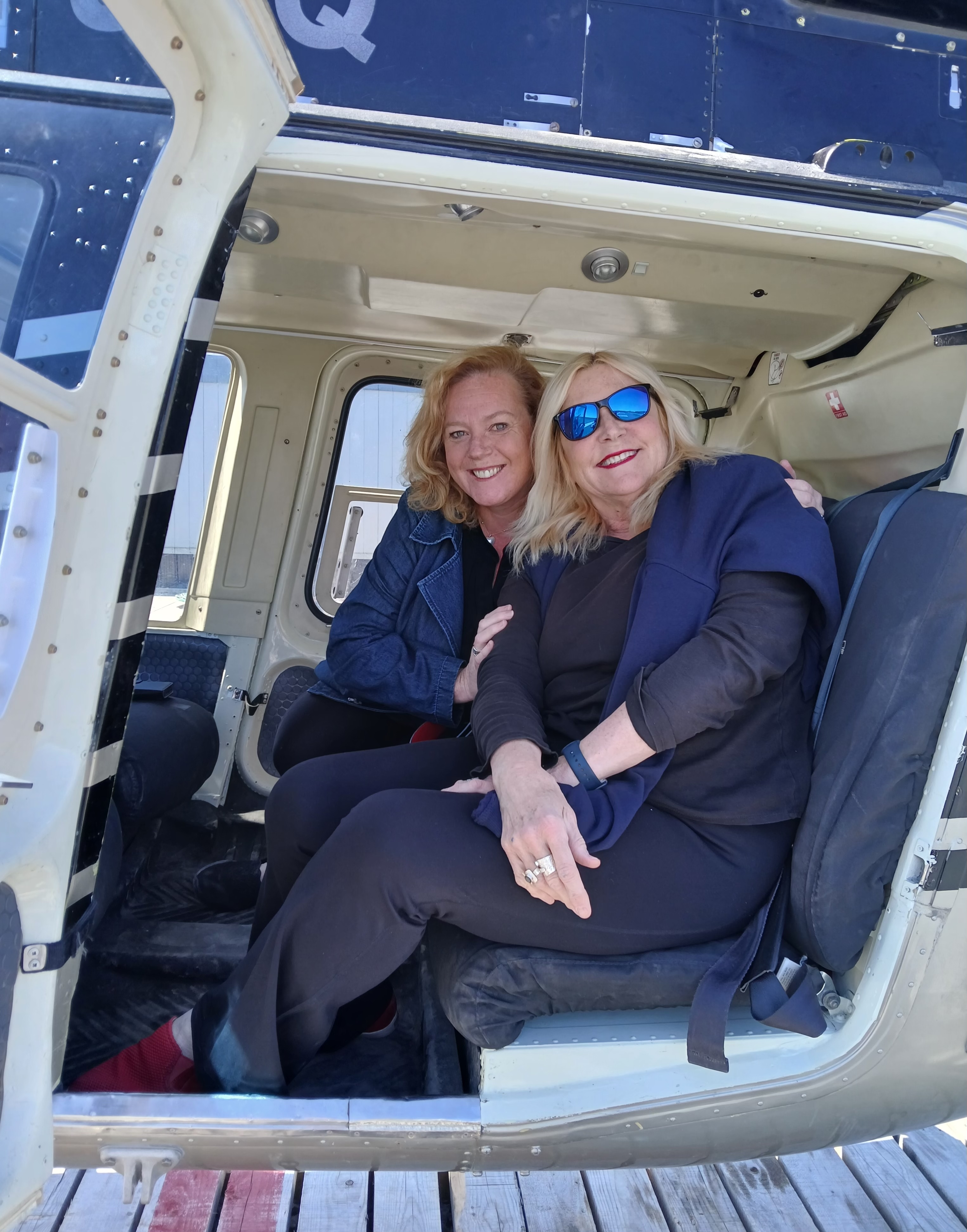 Lisa MacLeod and Susan Truppe smile from the back of a helicopter on their way between Moosenee and Cochrane.