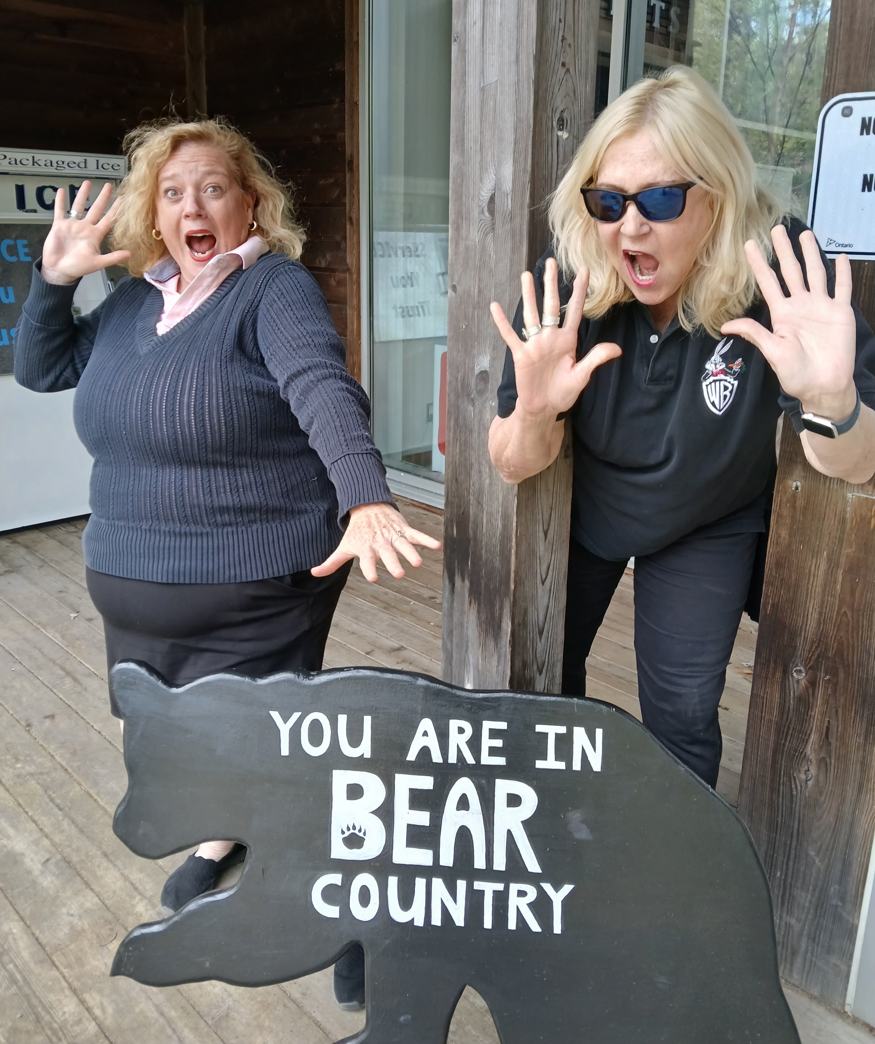 Lisa MacLeod and Susan Truppe pose with exaggerated expressions of fear as they stand next to a bear-shaped cutout that reads "You are in Bear Country".