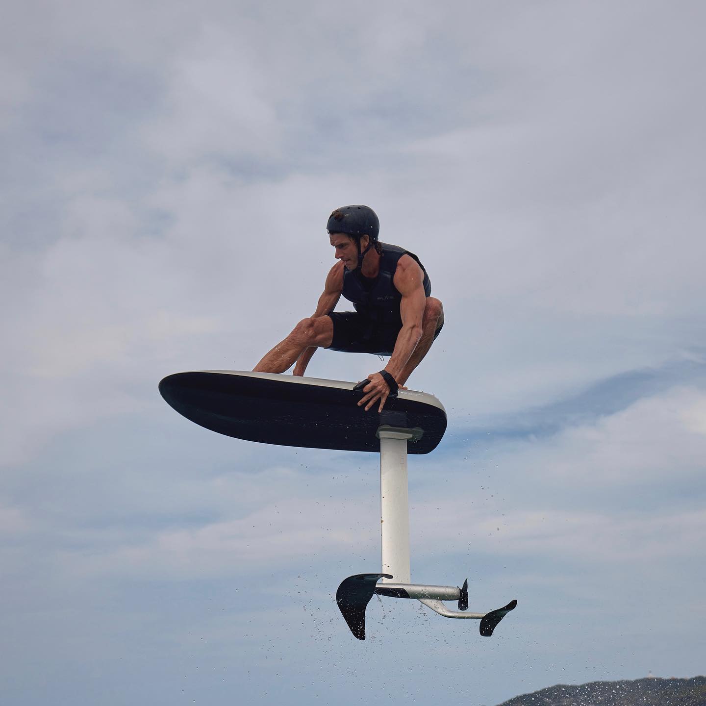 a rider on a hydrofoil jumps high above a lake.