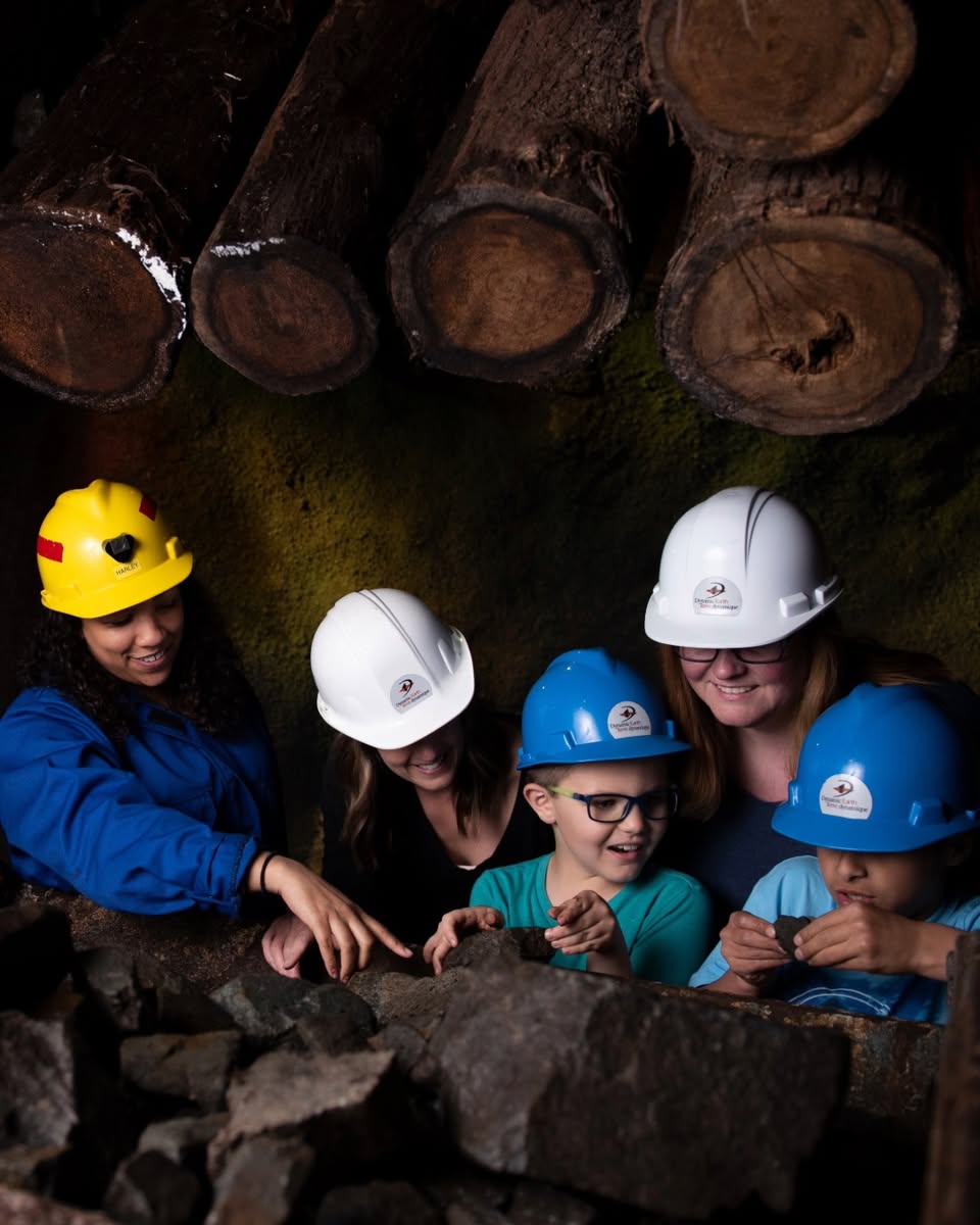 a group of smiling children learn about rock formations with some parents and guides in an underground tunnel.