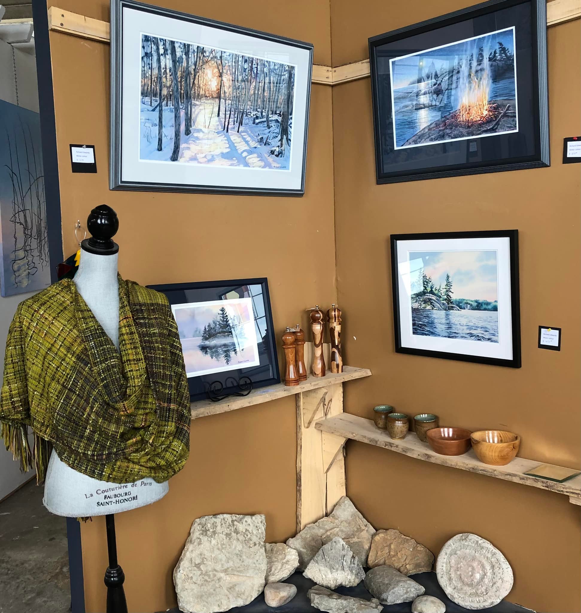 An arrangement of paintings featuring landscape scenes, handcrafted wooden bowls and a fine handwoven shawl on display in Edwards Art Studio.