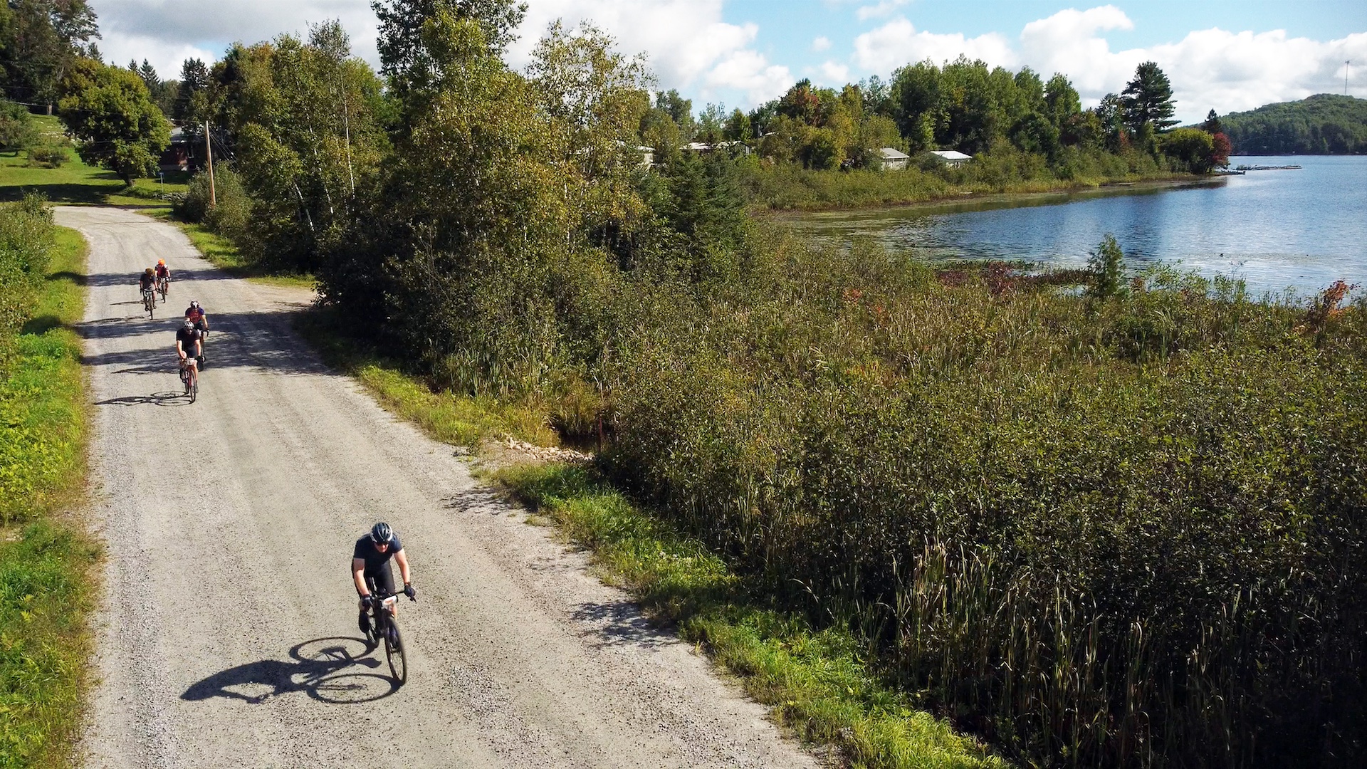 People riding bikes on gravel road beside a lake
