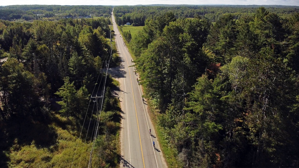 Overhead shot of cyclists on paved road with forest on either side